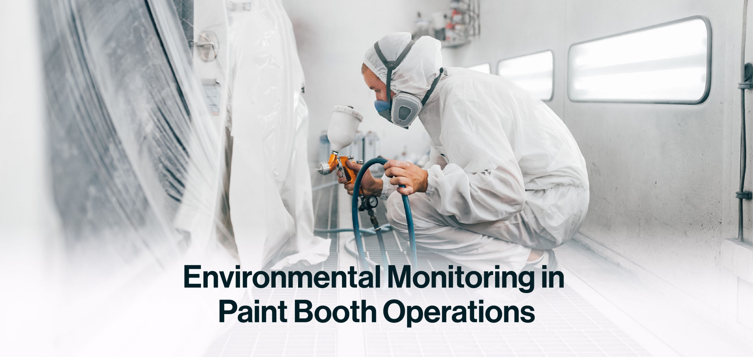 Worker in full protective suit and respirator operating a spray gun inside a paint booth to apply coatings